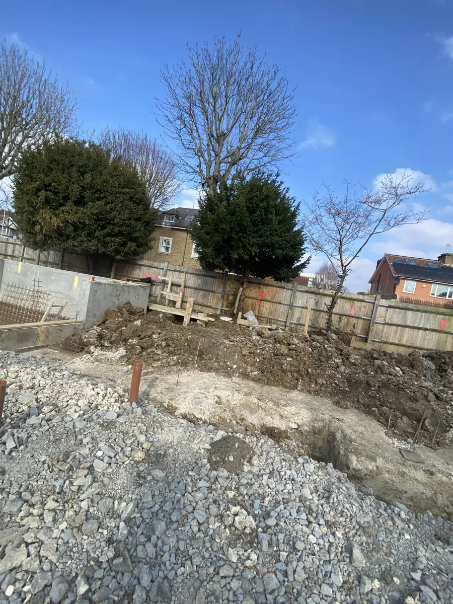 Bulk excavation and dug trenches beside a completed basement wall section with rebar mesh
