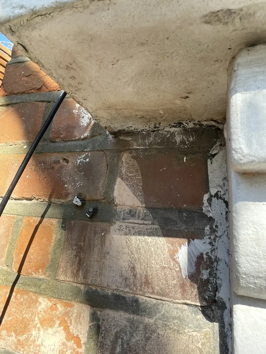Close-up of cracked brickwork below a stone sill with crack-monitoring studs fixed across the crack