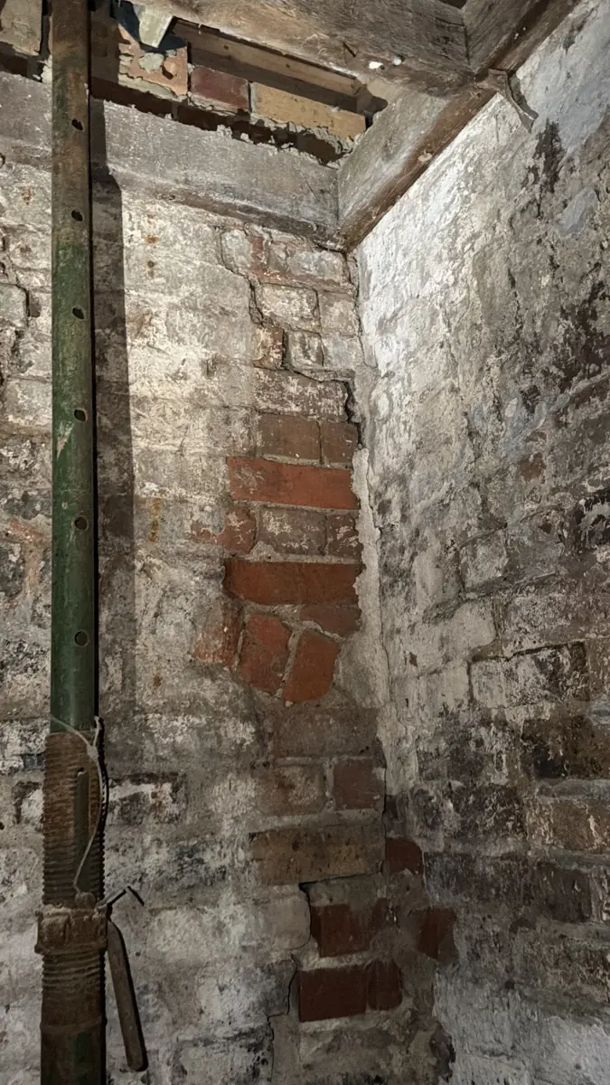 Basement vault with an acrow prop and stepped cracking and patch-repaired brickwork at the wall junction