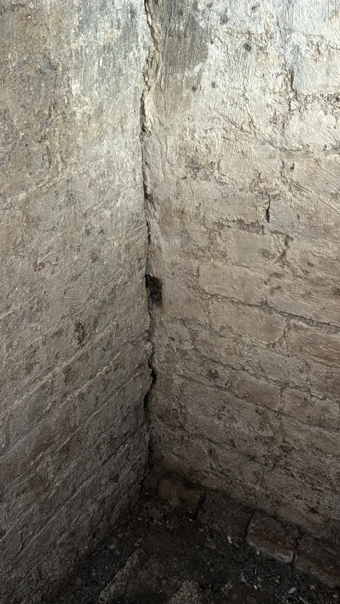 Vertical crack at an internal corner of a lime-washed basement wall