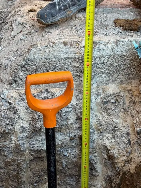 Close-up of exposed concrete footing in trial pit with tape measure
