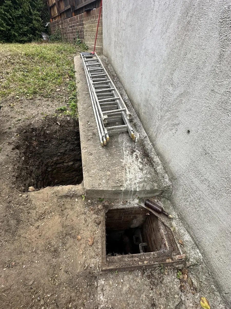 Trial pit dug beside a concrete retaining wall/ground beam with an open brick inspection chamber - investigating the unapproved works