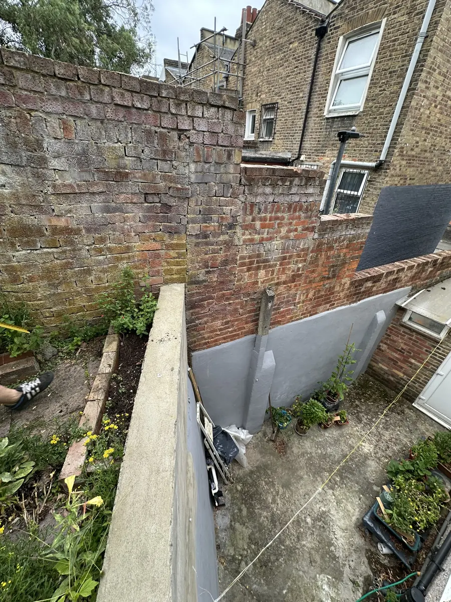Rear yard with the retrospectively built rendered retaining wall and concrete buttress posts against old brick boundary walls