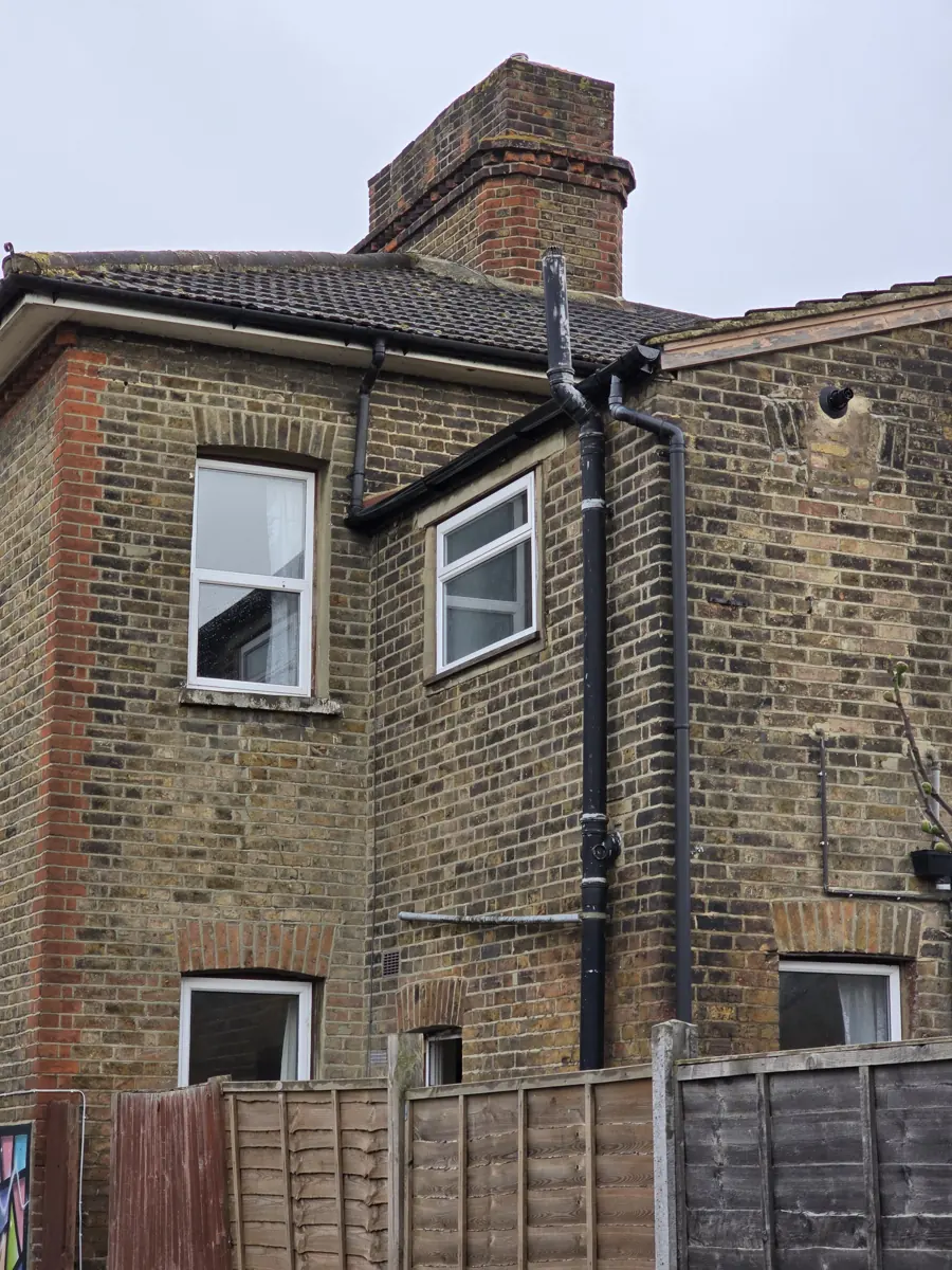 Close view of rear elevation brickwork, chimney stack and rainwater pipes above fence line
