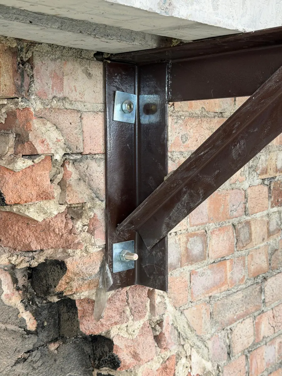 Close-up of a bolted steel angle gallows bracket supporting the retained chimney