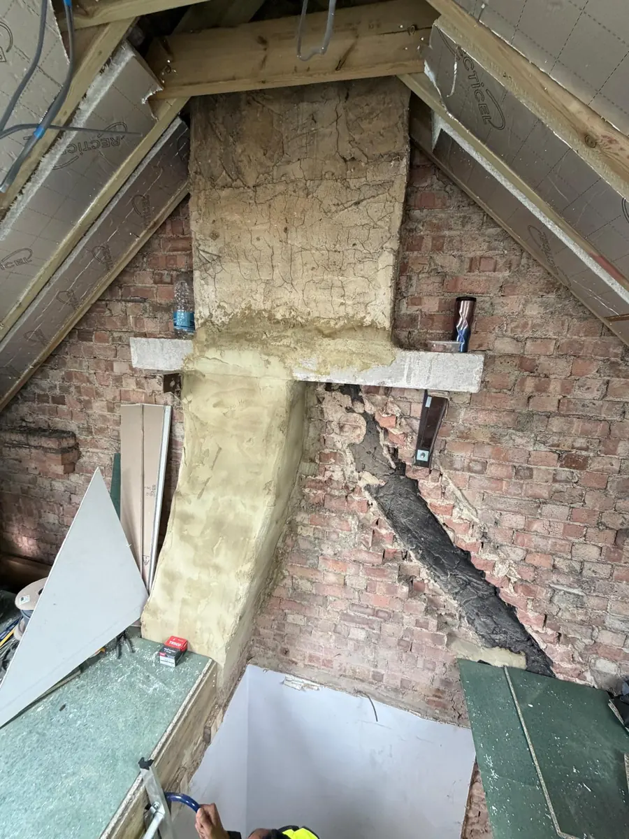 Loft under conversion: chimney stack carried on a concrete lintel and steel gallows brackets after the breast below was removed, with insulated rafters