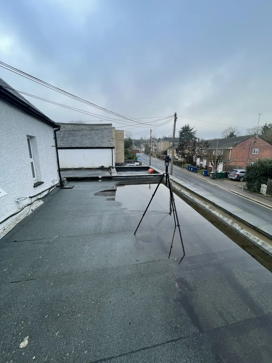 Survey of the existing flat roof over the ground-floor commercial frontage, with scanner tripod, parapet and the street running away